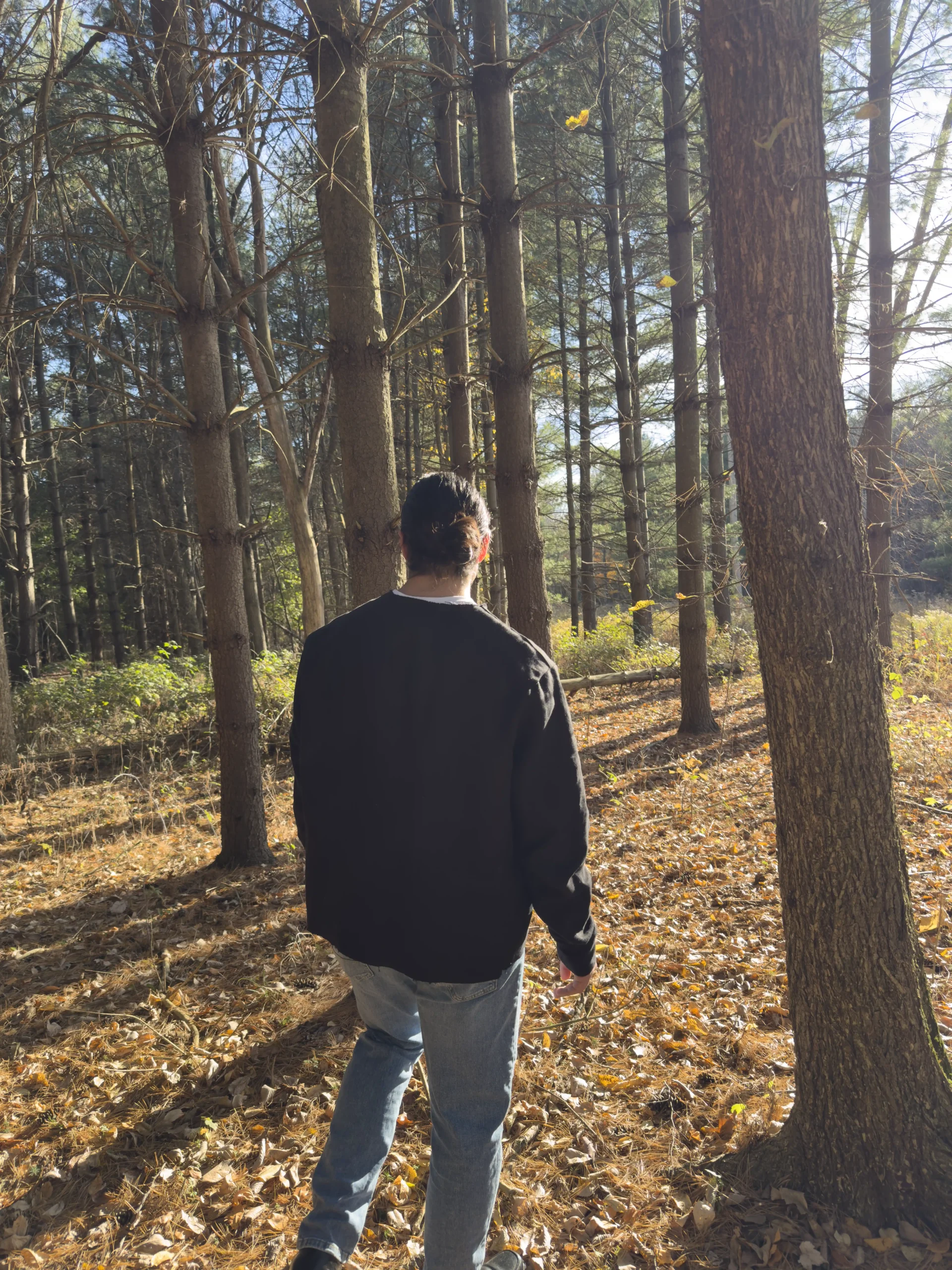 Anthony Mikinka wearing the black StructuredDenim Hemp Coat, photographed from behind in a wooded setting, showcasing the coat’s rugged, eco-friendly design.